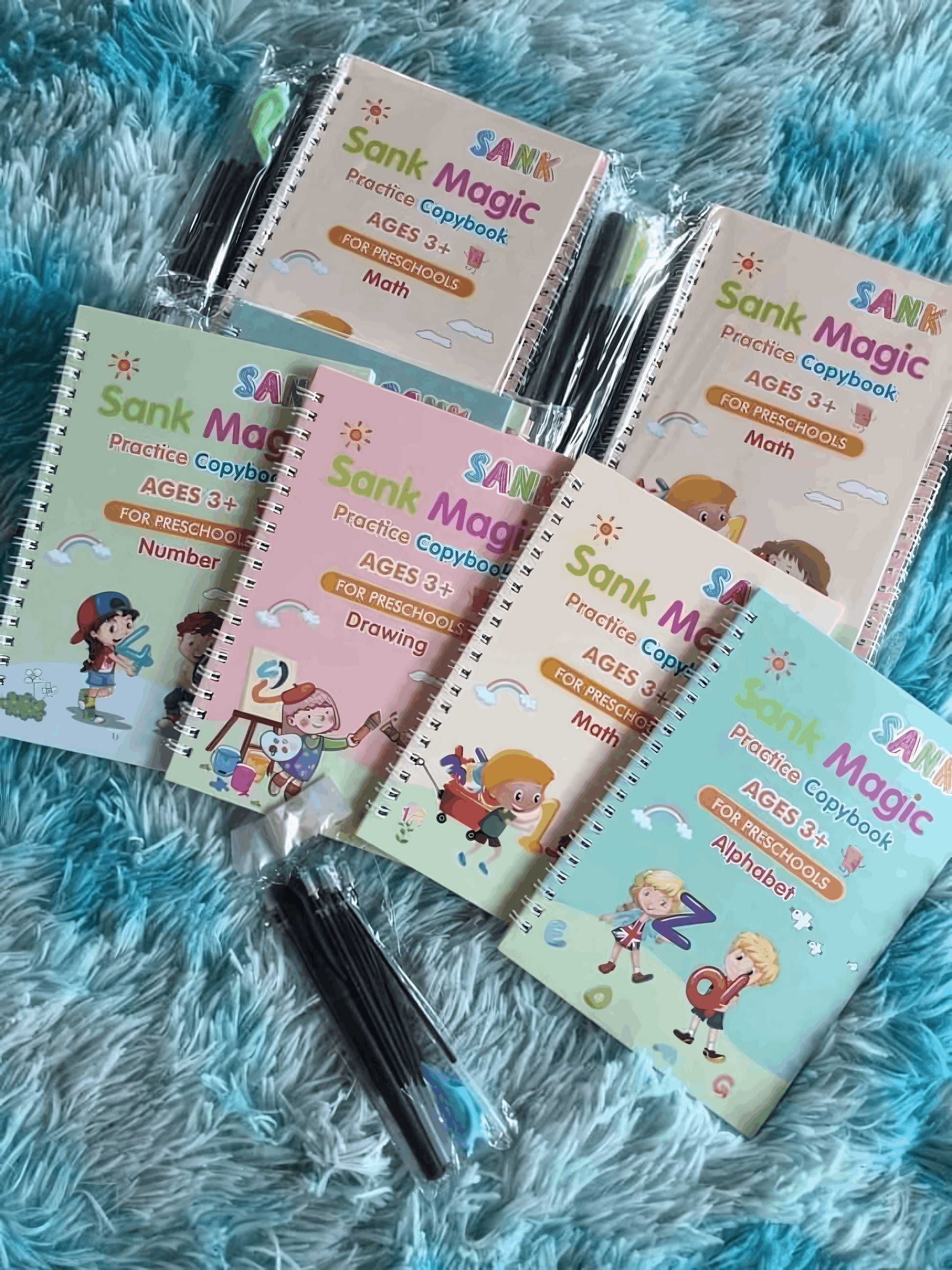 Set of Sank Magic practice copybooks with pens on a blue textured surface